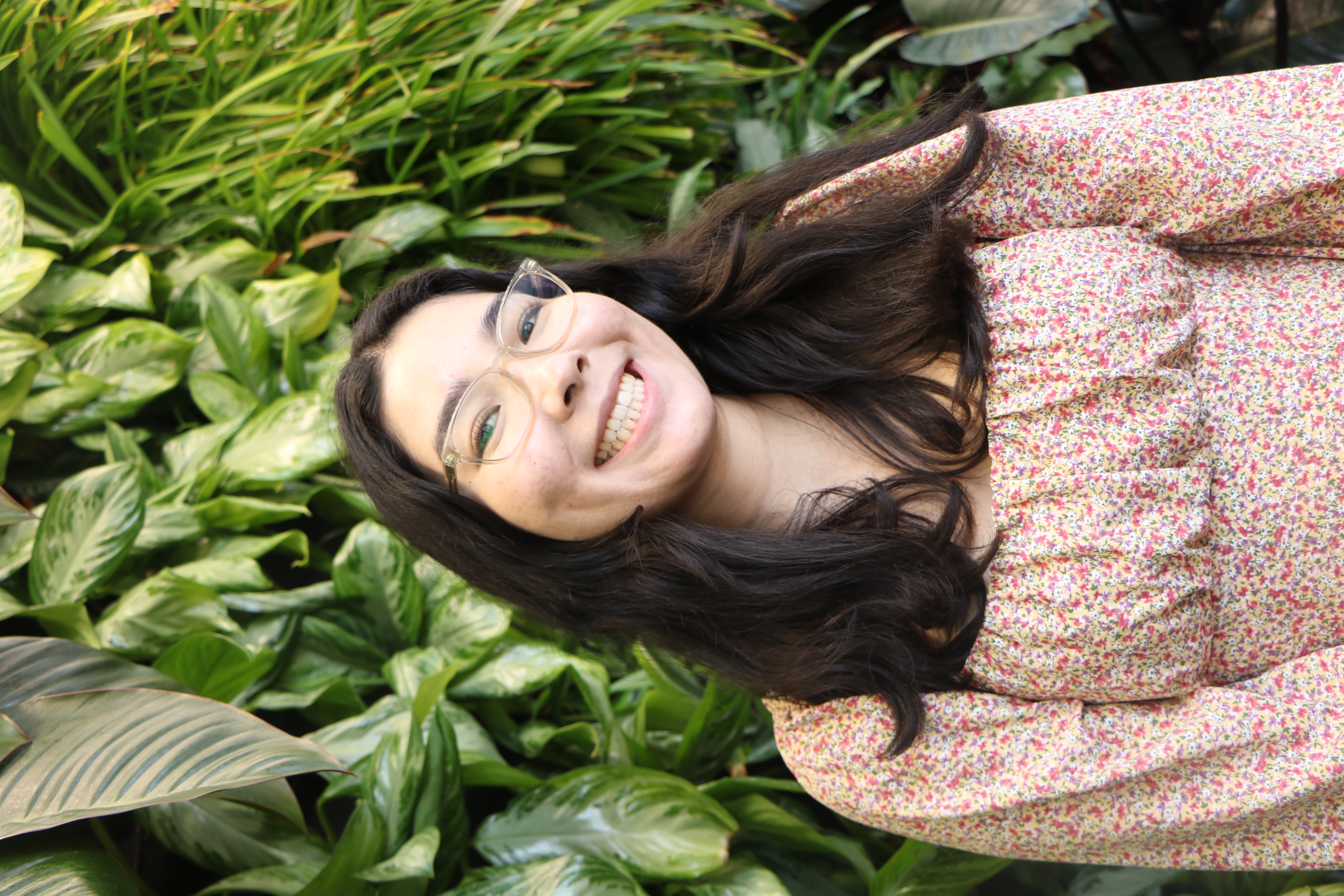 Photo of Ava Lamberty wearing a floral shirt in front of a greenery wall.